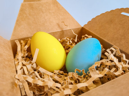 Inside a box filled with shredded paper, there are two colorful easter eggs hidden among the mess,...