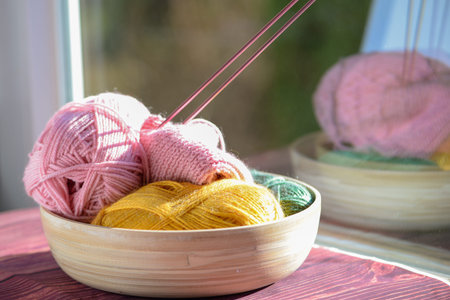 A tranquil and serene scene featuring a bowl filled with colorful yarn and knitting needles placed...