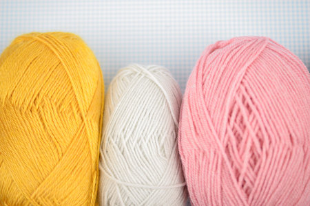 Three colorful yarn balls in bright yellow, soft white, and lovely pink, ideal for knitting and...