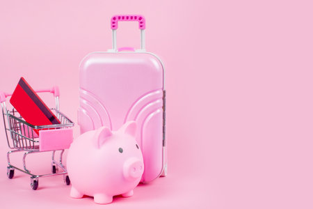 A vibrant setup featuring a pink suitcase, piggy bank, and shopping cart, symbolizing travel savings.の写真素材