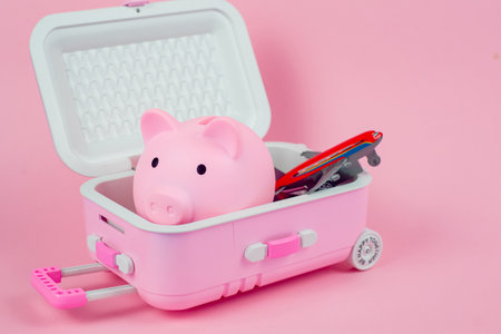 This is a charming piggy bank designed like a mini suitcase, vibrant and fun, set against a soft pink backgroundの写真素材