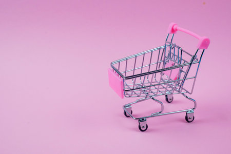A chic and stylish mini shopping cart set against a vibrant, lively pink backdrop, ideal for various retail themesの写真素材