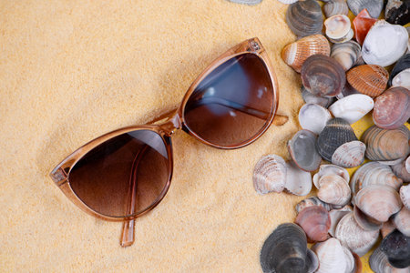 Sunglasses resting on warm sand, surrounded by beautiful seashells, create a perfect summer vibe atmosphereの写真素材