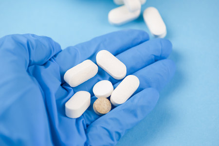 Closeup of medical worker or pharmacist hands wearing blue latex protective gloves,pouring white medicine pills on palm of handの写真素材