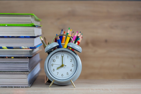 A charming desk setup includes a colorful alarm clock and a neat stack of books beside vibrant pencilsの写真素材