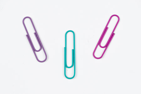 Three vibrant and colorful paper clips in purple, teal, and pink are nicely arranged on a pristine white surfaceの写真素材