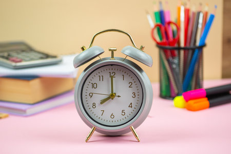 A classic alarm clock placed among vibrant school supplies, various books, and an array of colorful stationery itemsの写真素材
