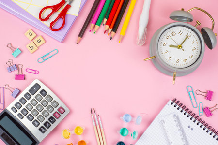 A collection of vibrant office supplies, such as scissors, a clock, and a calculator, displayed against a pink backdropの写真素材