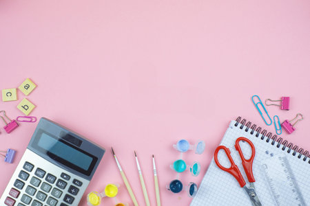 An assortment of colorful stationery items including scissors, calculator, and notepad on a pink...