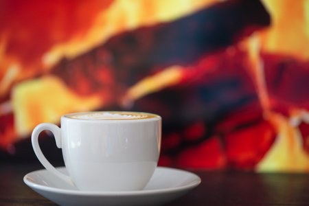 A steaming cup of rich coffee beautifully sets the cozy mood beside a vibrant background of glowing, warm embersの写真素材