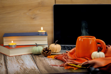 A cozy autumn scene with a warm drink, flickering candles, books, and decorative pumpkins for seasonal charmの写真素材