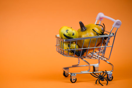 A vibrant shopping cart filled with Halloween-themed pumpkins and spiders, perfect for spooky vibes.の写真素材