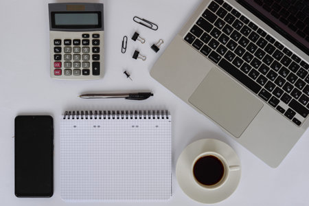A neatly organized and clean workspace showcases a laptop, calculator, notebook, and a steaming...