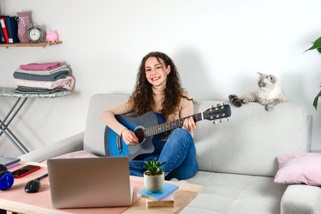 A Young Woman is Joyfully Playing the Guitar at Home with Her Beloved Cat by Her Side
