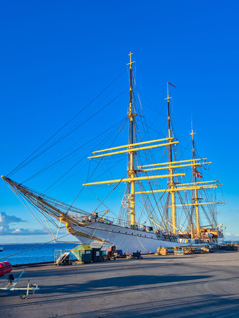 A stunning tall ship adorned with sails, elegantly moored against a captivating vibrant blue sky...