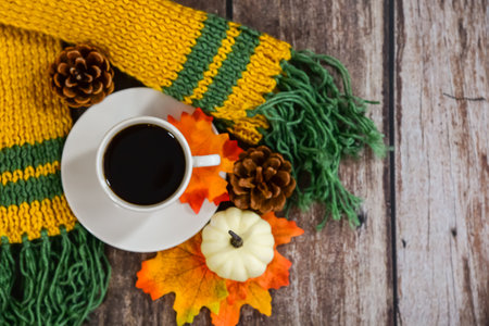 A cozy autumn scene with a ceramic mug of coffee on a knitted scarf, surrounded by golden leaves. Perfect for depicting warmth, relaxation, and seasonal comfort in fall settings. High quality photoの写真素材