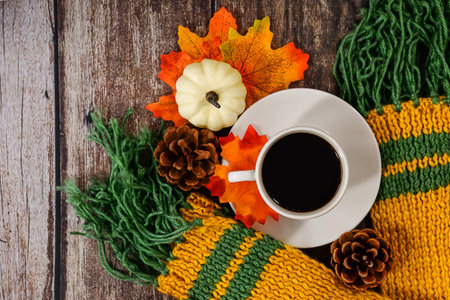 A cozy autumn scene with a ceramic mug of coffee on a knitted scarf, surrounded by golden leaves....