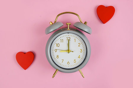 vintage alarm clock with red hearts, on pastel pink surface, symbolic valentines timing and...