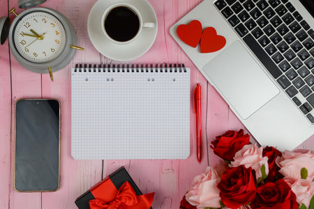 alarm clock beside coffee and laptop, pink desk with notepad, phone and red hearts, gift box with ribbon,の写真素材