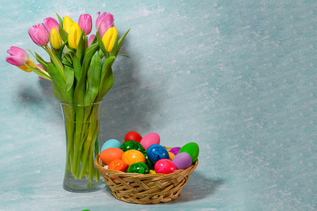 Tulips in a vase and a basket of Easter eggs on a blue background with space for text