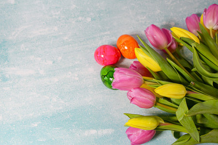 Easter celebration concept. Top view photo of colorful easter eggs yellow and pink tulips on pastel background with copyspaceの写真素材