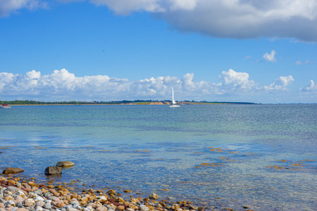 Small Sailboat On Serene Bay With Distant Horizon And Calm Water, Single White Sail Punctuating...