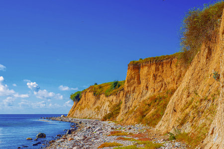Elevated Rugged Cliff Overlooking Shimmering Shoreline. Striking Promontory With Weathered Rocks Beside Calm Azure Watersの写真素材