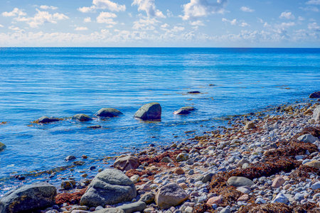 Calm Shoreline Featuring Rounded Stones And Bright Sky. Peaceful Natural Seascape With Smooth Rocks And Clear Blue Watersの写真素材