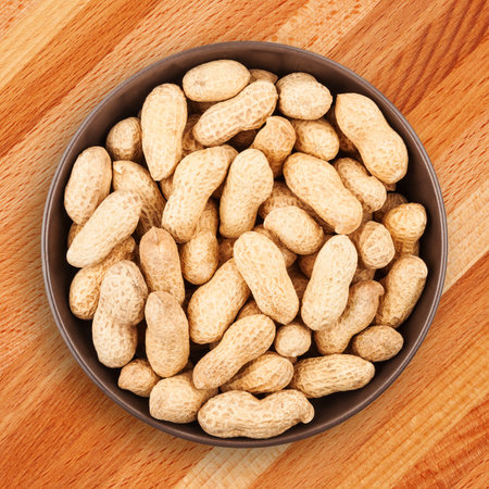 Delicious and healthy snack. Unshelled peanuts in ceramic bowl on wooden background closeup, top...