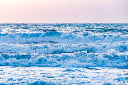 Photo of the sea waves on the background of sunrise or sunset. The sky in a beautiful gold, blue, light blue and orange colors.の写真素材