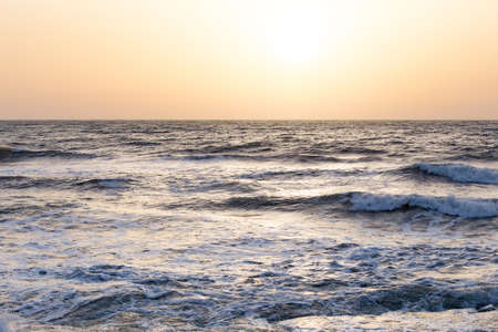 Photo of the sea waves on the background of sunrise or sunset. The sky in a beautiful gold, blue, light blue and orange colors.の写真素材