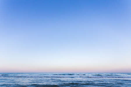 Photo of the sea waves on the background of sunrise or sunset. The sky in a beautiful gold, blue, light blue and orange colors.の写真素材