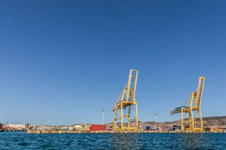 Photo Sea port with a dock, where stands large yellow crane. On the background you can see a lot of blue, red, yellow and gray containers.の写真素材