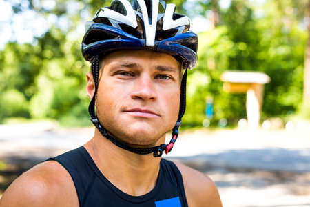 Professional cyclist smiling with helmet head for safety in front of the competition. Snap buttoned under the neck. Bicycle helmet blue with white, in the morning in the green forest.の写真素材