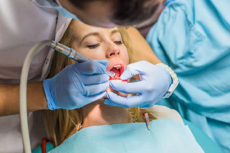 Attractive blond girl having her teeth examined at a dental surgery by a dentist or stomatologist, close up view of her face and the dentists gloved hands with instrumentsの写真素材