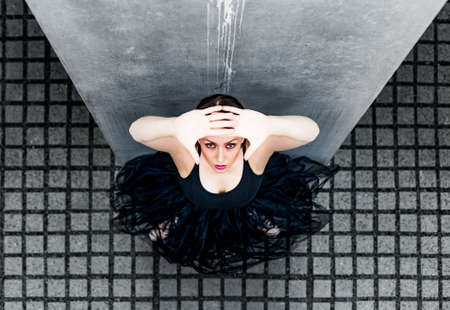 ballerina looking up against the gray tiles and slabs of concrete. around are gray concrete steles that sivoliziruyut concrete cityの写真素材