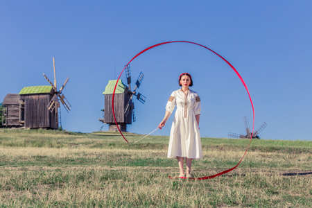 Girl dressed in traditional ethnic costume stands on a background field with windmills. it makes a circle of red tapeの写真素材
