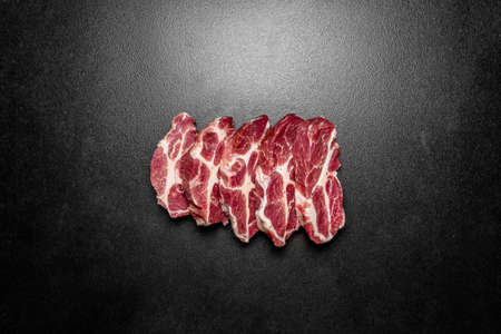 Overhead view raw pieces of pork on black background. Pieces of fresh boneless pork, neck part or collar. Pieces of red raw meat on a black backgroundの写真素材