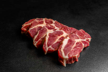Close up pieces of raw pork isolated on black background. Pieces of fresh boneless pork, neck part or collar. Pieces of red raw meat on a black backgroundの写真素材