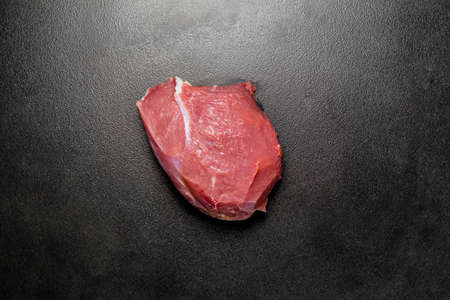 Overhead view eyes round beef meat on black background. Piece of fresh raw beef. Big piece of red meat on a dark textured ceramic backgroundの写真素材