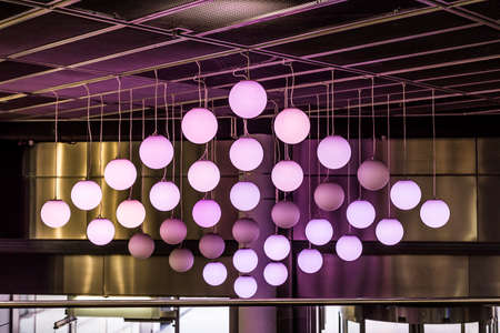 Installation of round lamps on the ceiling. Spherical violet lamps hanging on the wall of the city buildings.の写真素材