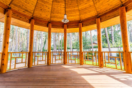 Large semi-circular porch in warm ecological wooden house with a garden view. On the ceiling hanging lamp. Porch is made of brown oak tree.の写真素材