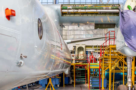 Back view of white aircraft stands on repair in aviation hangar. Airplane without wing placed in front of yellow gate of the shed.の写真素材