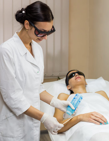 Beautician preparation for epilation laser treatment to beautiful brunet girl. Cosmetologist in...