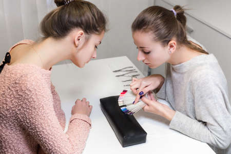 Before manicure process beautiful girl choice of color nail polish in beauty salon.Client sit at the table and look color palette near the master.の写真素材
