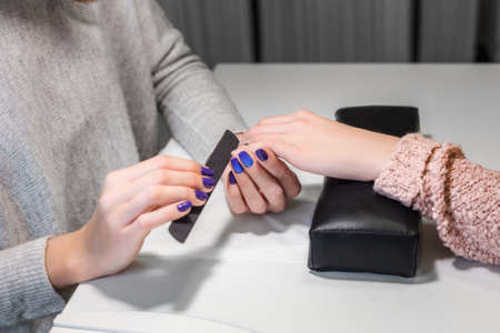 Processing nails with emery nail-file in beauty nail salon.Client receiving manicure by beautician. Gentle care of nails in cosmetic salon. Nail file. Manicure process.の写真素材