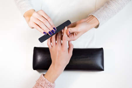 Top view manicurist polishing index finger for manicure in nail beauty salon. Step of manicure process.の写真素材