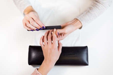 Top view manicure master nail file works on the pointing finger.Process of polishing fingers on towel in beauty salon.の写真素材