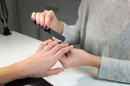 Professional process of manicure by nail file in white beauty salon.Manicurist gently manicured service. Hand on the black professional pillow.の写真素材