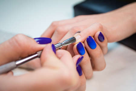 Manicurist removing cuticle from the girl client nail at beauty salon. Master with beautiful blue shellac manicure.の写真素材